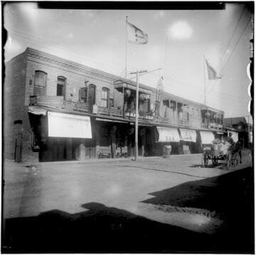 Street scene of storefronts and horse-drawn wagon